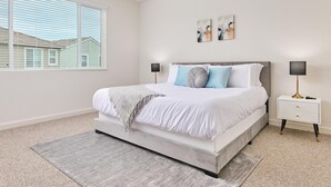Een slaapkamer met een groot bed, twee nachtkastjes, een raam met zonwering en twee aan de muur bevestigde kunstwerken.