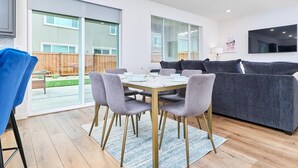 Een moderne woonkamer met een eettafel, grijze banken en een aan de muur bevestigde televisie.