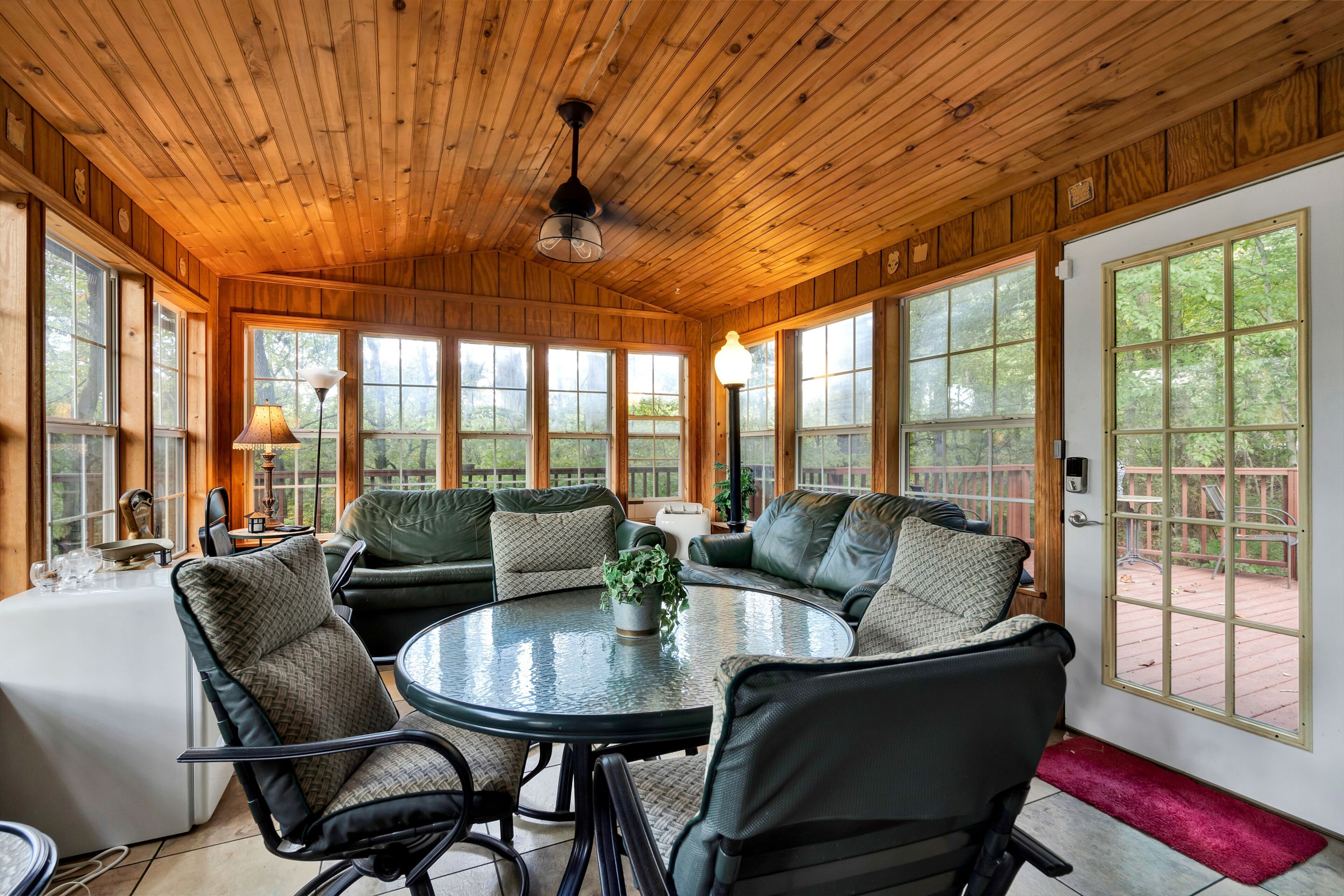 A sunroom with a wooden ceiling, large windows, and a round table with chairs.