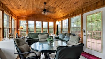 A sunroom with a wooden ceiling, large windows, and a round table with chairs.