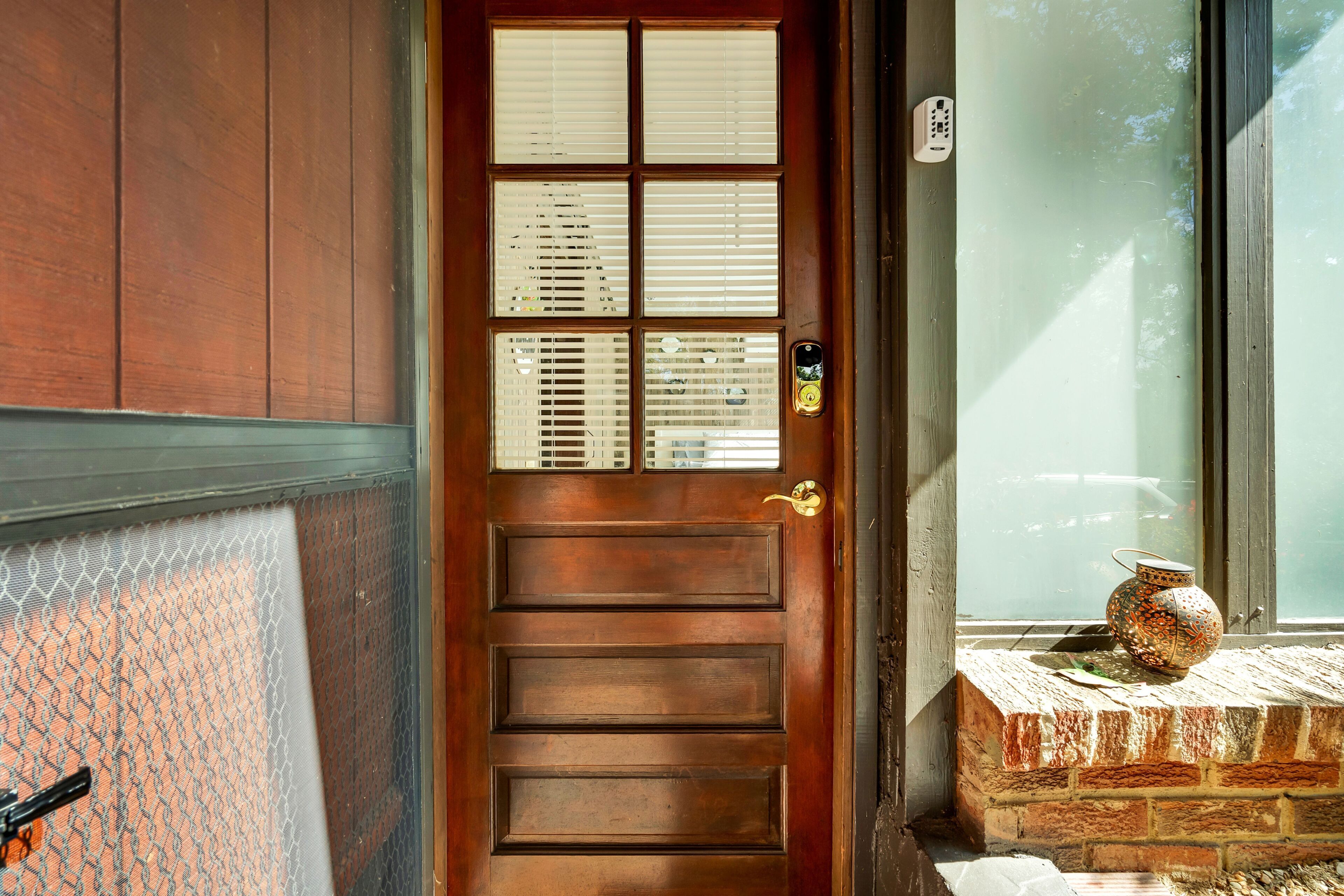 A wooden door with a window, a keypad lock, and a small decorative pot on a brick ledge.