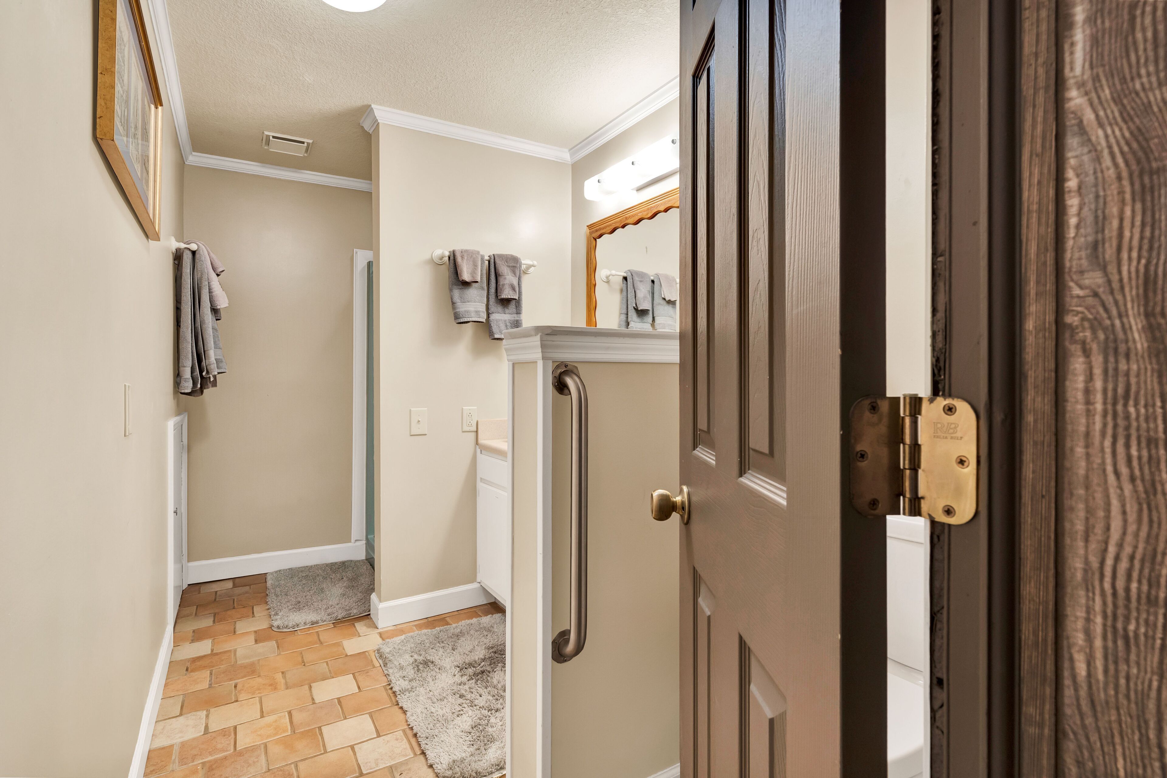 A hallway with a wooden door, a white wall, a mirror, and a towel rack.