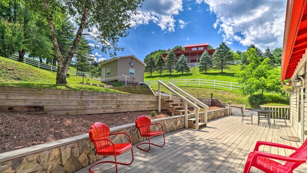 A wooden deck with red chairs, a stone retaining wall, and a view of a building with a clock. - Fish, Float & Relax Fireside: Home Near New River! (Crumpler)