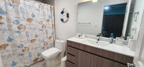 A bathroom with a shower curtain featuring sea life patterns, a toilet, a sink with a mirror, and a towel rack.