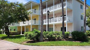 Un edificio de varios pisos con balcones, un camino de entrada pavimentado y jardines bien cuidados.