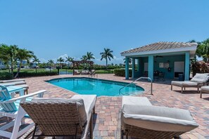 Ein Poolbereich mit Liegestühlen, einem überdachten Sitzbereich und blauem Himmel.