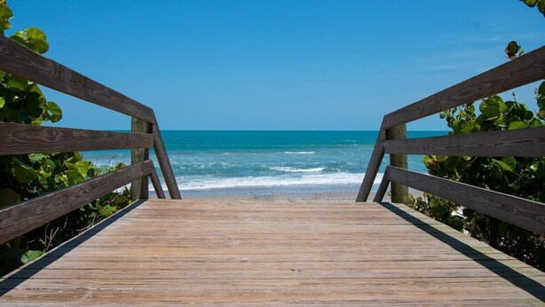 Una pasarela de madera que lleva a una playa con agua azul cristalina y cielo despejado.