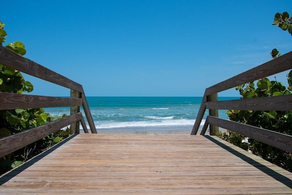 A wooden boardwalk leading to a beach with clear blue water and a clear sky.