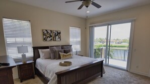 Un dormitorio con cama, mesita de noche, lámpara, ventilador de techo y balcón con vistas.