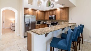 Una cocina con una isla central, armarios de madera, electrodomésticos de acero inoxidable y taburetes de bar azules.