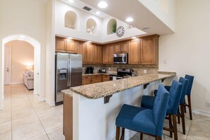 A kitchen with a central island, wooden cabinets, stainless steel appliances, and blue bar stools.