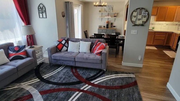 Un salon avec un canapé gris, un tapis à motifs et un coin repas agrémenté d’un lustre.