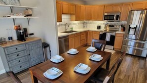 Une cuisine moderne avec des meubles en bois, des appareils en acier inoxydable et une table à manger pour quatre personnes.