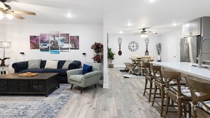 Un soggiorno moderno con un tavolino da caffè scuro, un divano blu e un'area pranzo con sedie di legno e un tavolo bianco.