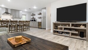 Un soggiorno moderno con un tavolino da caffè in legno scuro, una televisione a schermo piatto su un supporto in legno e una cucina sullo sfondo.