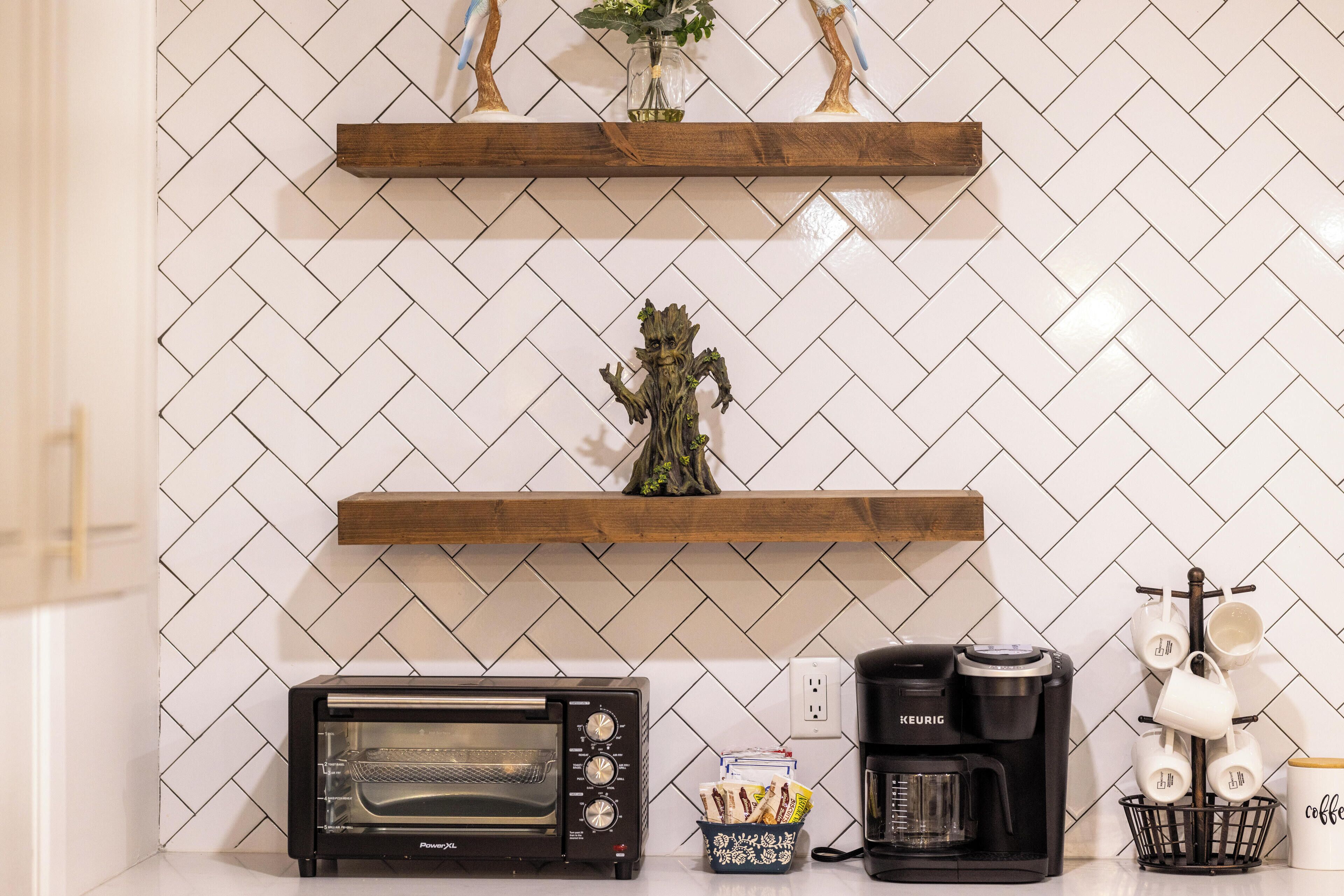 A kitchen with a herringbone tile backsplash, a toaster oven, a coffee maker, and a basket with utensils.