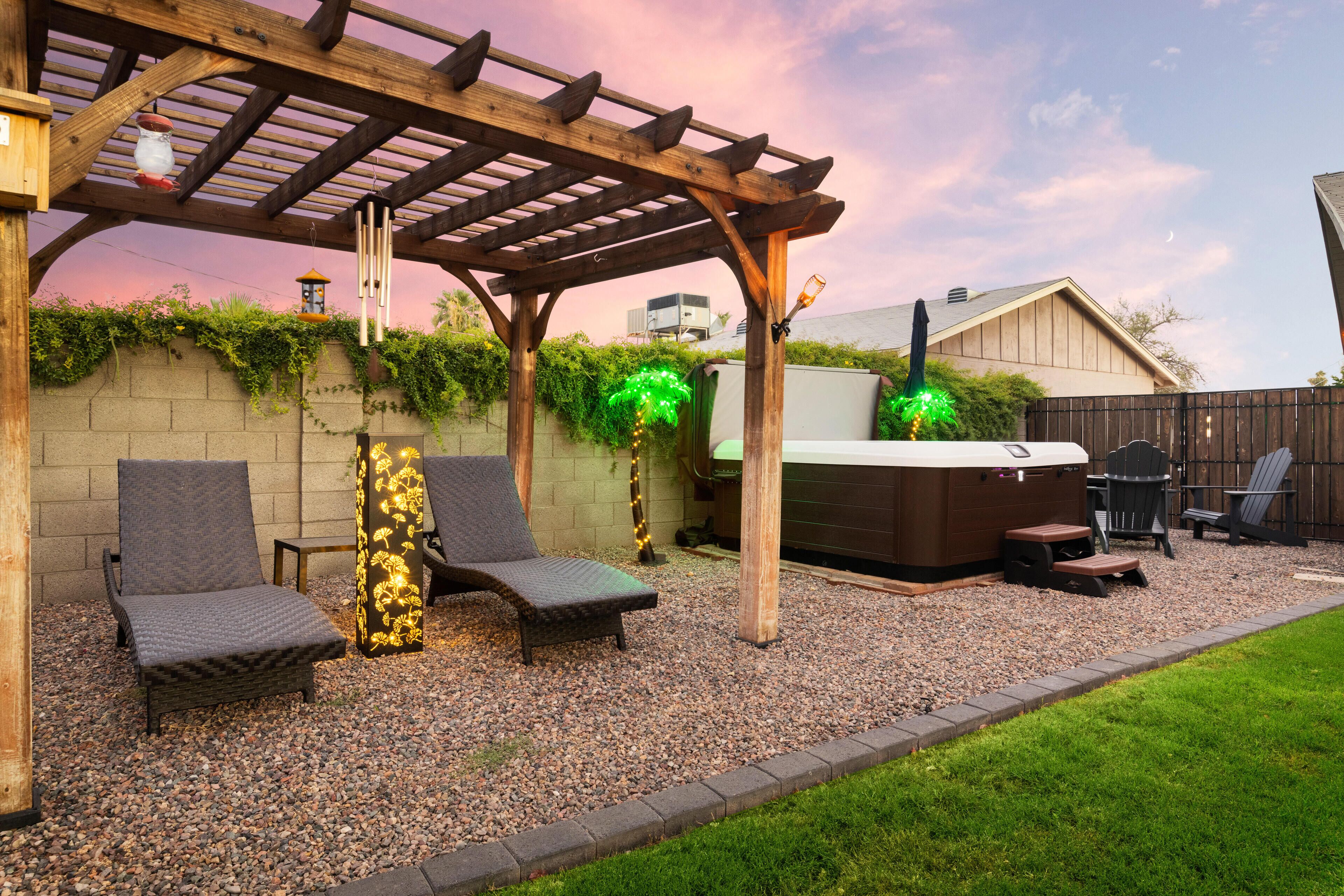 A covered patio area with two lounge chairs, a hot tub, and a wooden pergola.
