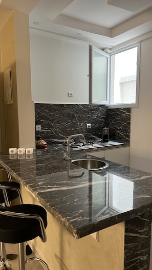 A modern kitchen with a marble countertop, stainless steel sink, and a window above the sink.