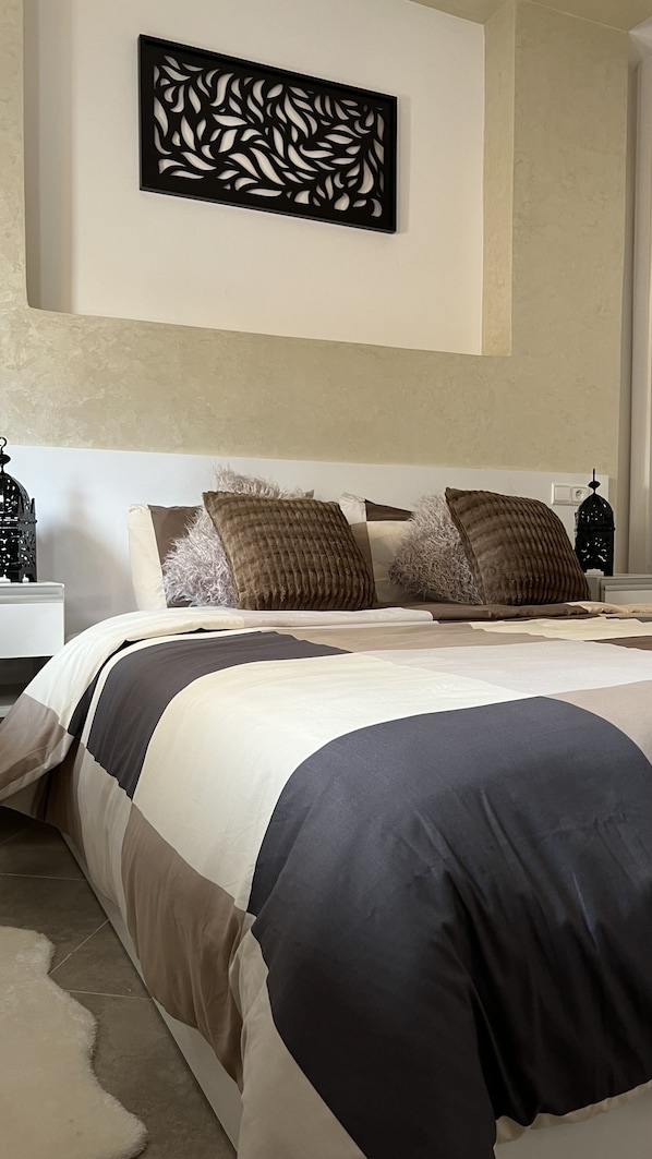 A neatly made bed with a dark and light striped bedspread, multiple pillows, and a decorative wall piece above it.