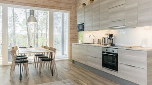 Moderni keittiö, jossa on puiset kaapit, ruokailutila pöydän ja tuolien kera sekä suuret ikkunat, joissa on sälekaihtimet.