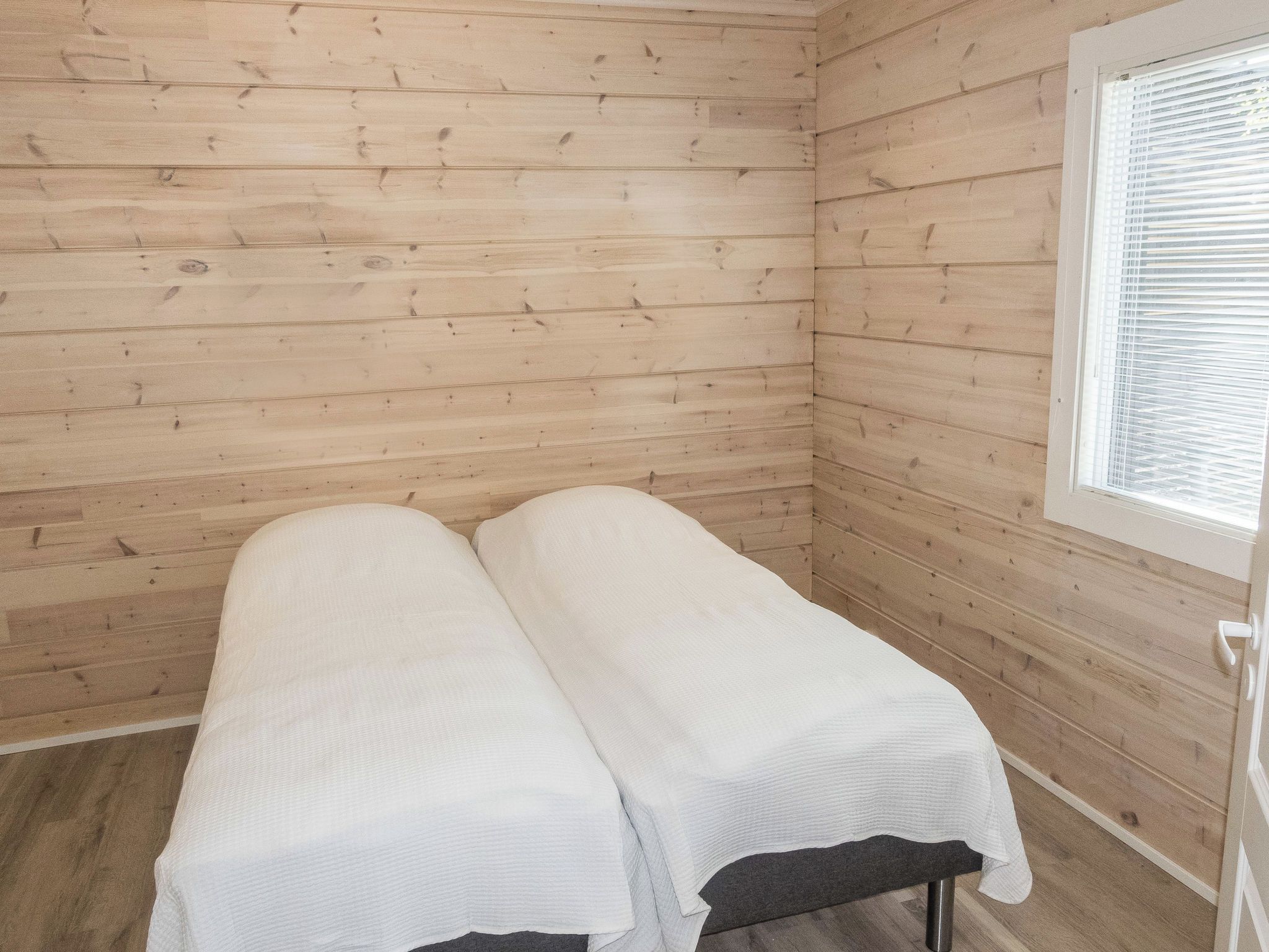 A small, single-occupancy room with wooden walls and a window with blinds.