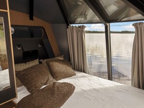 Une chambre à coucher avec un grand lit, une tête de lit et une vue sur un lac par la fenêtre.