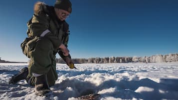 A person crouching on a snowy surface, holding a fishing rod.
