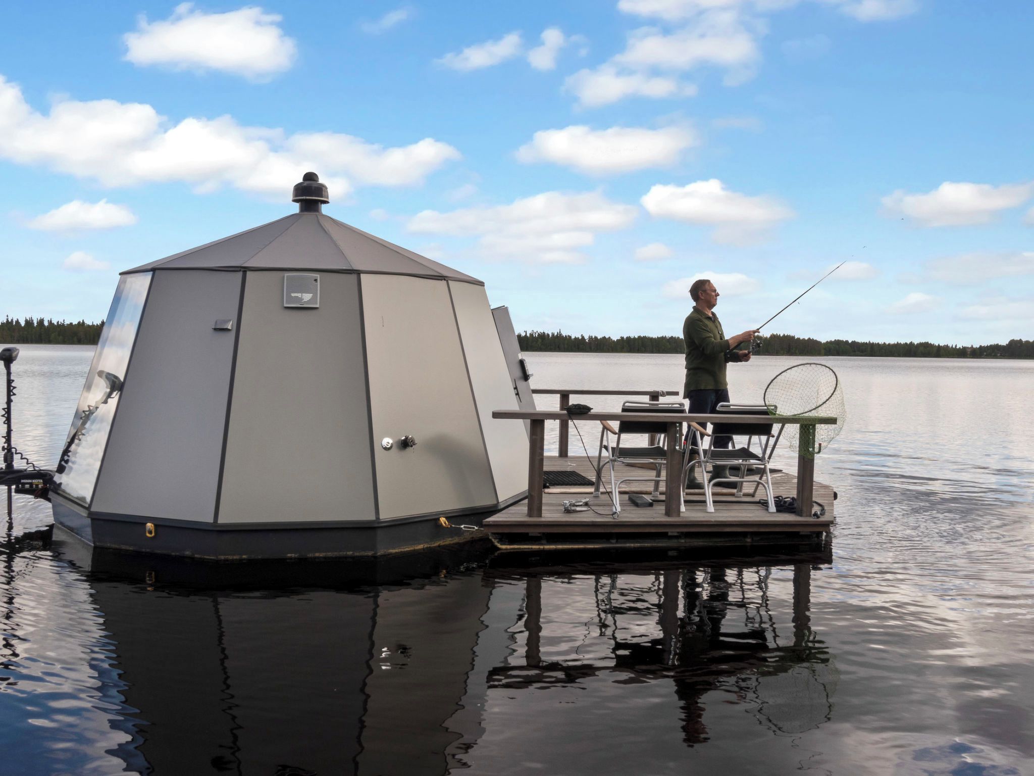 A stationary boat with a cabin, a fishing rod, and a chair on a calm lake.