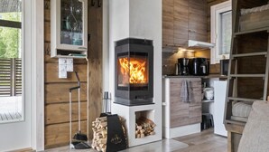 A cozy living room with a wood-burning stove, a kitchen area, and a dining space. - Lystikämän elämys by Interhome (Rovaniemi)