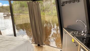 Ein kompaktes Zimmer mit Bett, einer Küchenzeile und Blick auf ein Gewässer durch ein Fenster.