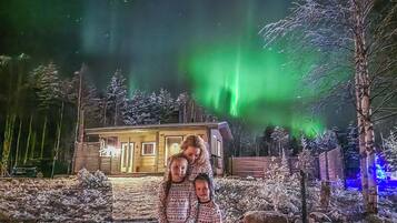 Een blokhut met een sneeuwbedekt landschap en een zichtbare poollichtshow op de achtergrond.