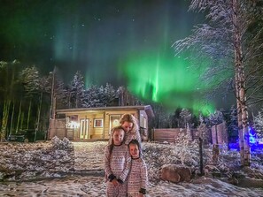 A cabin with a snow-covered landscape and a visible aurora display in the background.