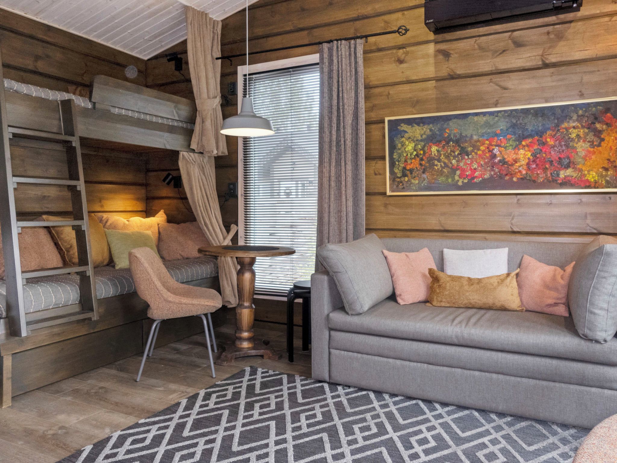 A cozy room with a bunk bed, a grey sofa, a patterned rug, and a painting on the wall.