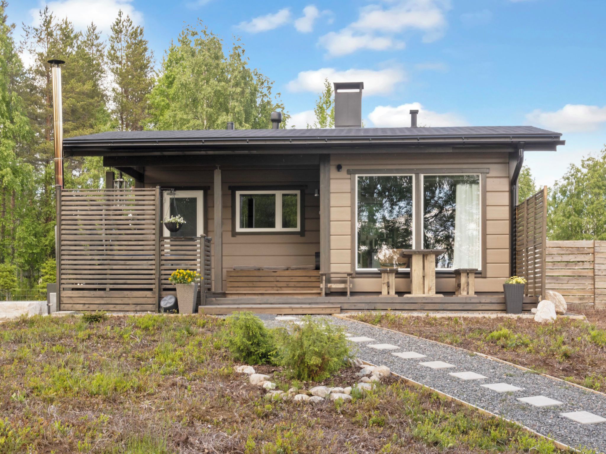A modern single-story house with a covered porch, large windows, and a stone pathway leading to the entrance.