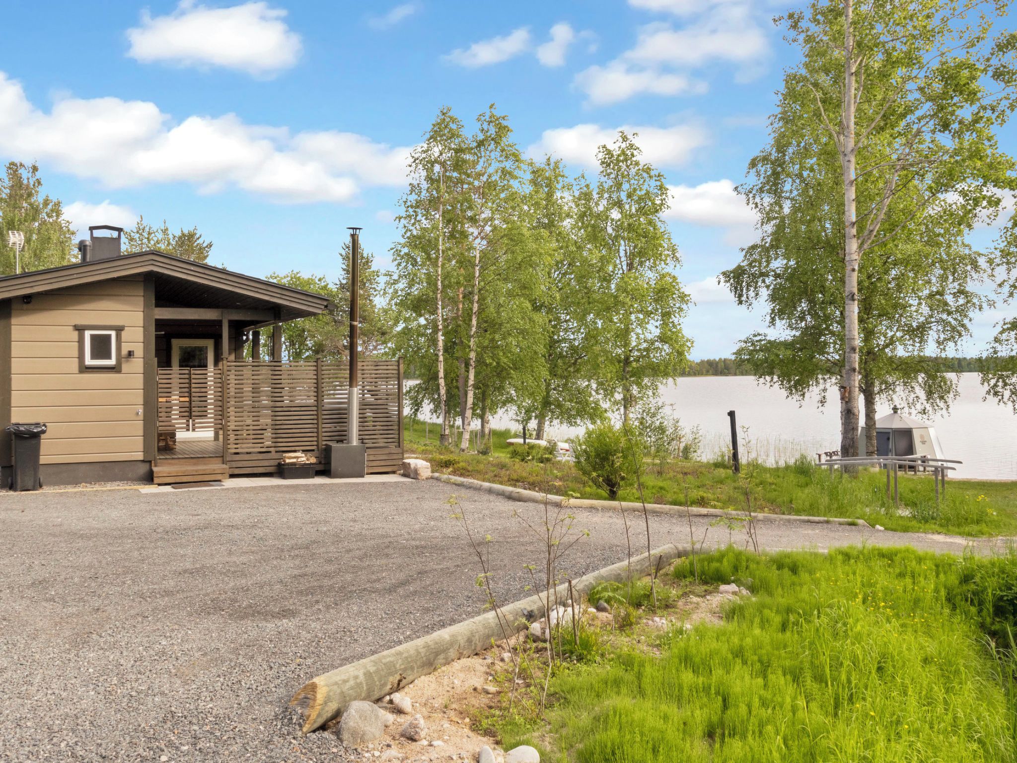 A cabin with a gravel driveway, a small porch, and a view of a lake.