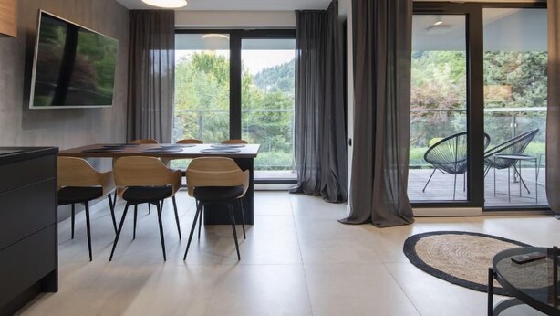 Ein moderner Essbereich mit großem Tisch und Stühlen, einem flachbildfernseher an der Wand und Blick auf einen See und Bäume durch große Fenster.