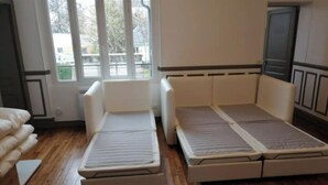 A room with a wooden floor, a white sofa, and a bed with a headboard.