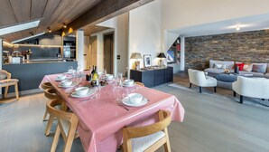 Uma sala de jantar com toalha xadrez vermelha, cadeiras de madeira e uma cozinha ao fundo.