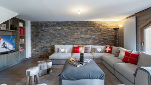 Uma sala de estar moderna com uma parede de pedra, um sofá modular cinza e uma TV de tela plana em uma estante de madeira.