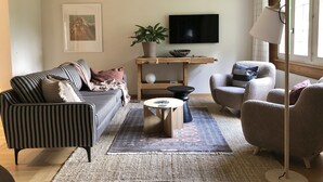 Un salon avec un canapé à rayures, une table basse ronde, un fauteuil gris et un téléviseur fixé au mur.