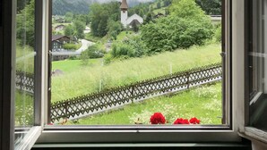Une vue par la fenêtre sur un paysage montagneux, avec une église, une végétation luxuriante et une voie ferrée.