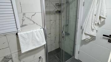 A bathroom with a glass-enclosed shower, a white towel hanging on the wall, and a tiled floor.