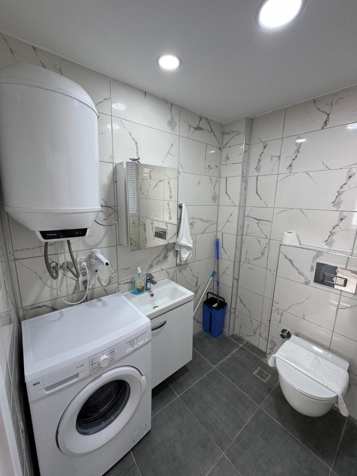 A bathroom with a washing machine, sink, toilet, and a mirror.