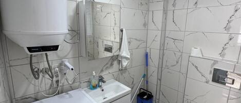 A bathroom with a washing machine, sink, toilet, and a mirror.