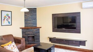 Un salon avec une cheminée en pierre, un téléviseur fixé au mur et un canapé en cuir marron.