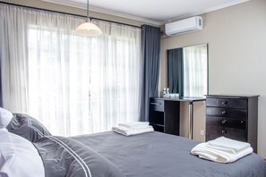 A hotel room with a bed, a desk, a dresser, and a window with curtains. - Inviting 3-bed Apartment In The City (Mutare)