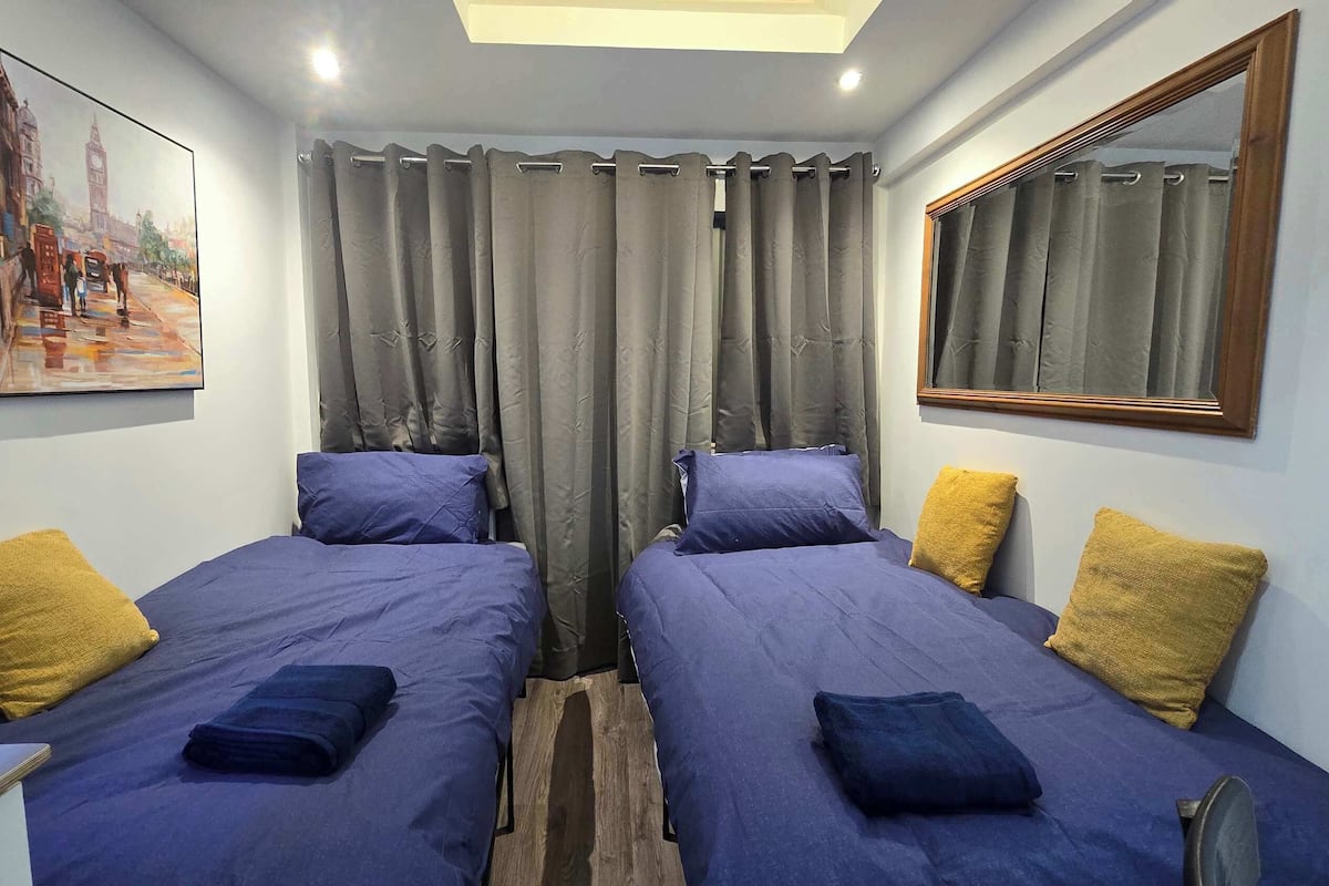 A room with two beds, grey curtains, a painting of a cityscape, and a mirror on the wall.