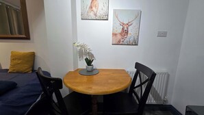 A small dining area with a round wooden table, two black chairs, a potted orchid, and a yellow pillow on a blue sofa. - Lopez Home Crawley (Crawley)