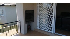 A balcony with a metal railing, a black grill, and a white security gate. - A home away from home (Mbombela)