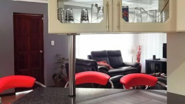 A dining area with a glass-fronted cabinet containing glassware, a black bar counter with red stools, and a black leather sofa in the background. - A home away from home (Mbombela)